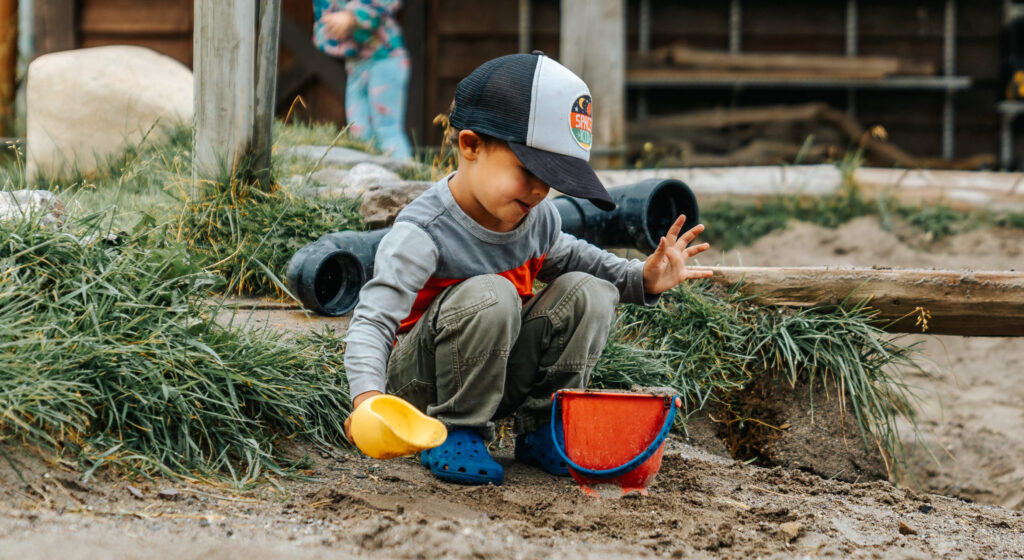 boy scooping up mud and sand into a pail