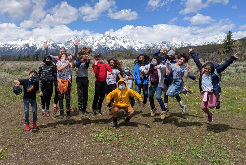 group of 5th-grade students jump for joy with the Tetons behind them